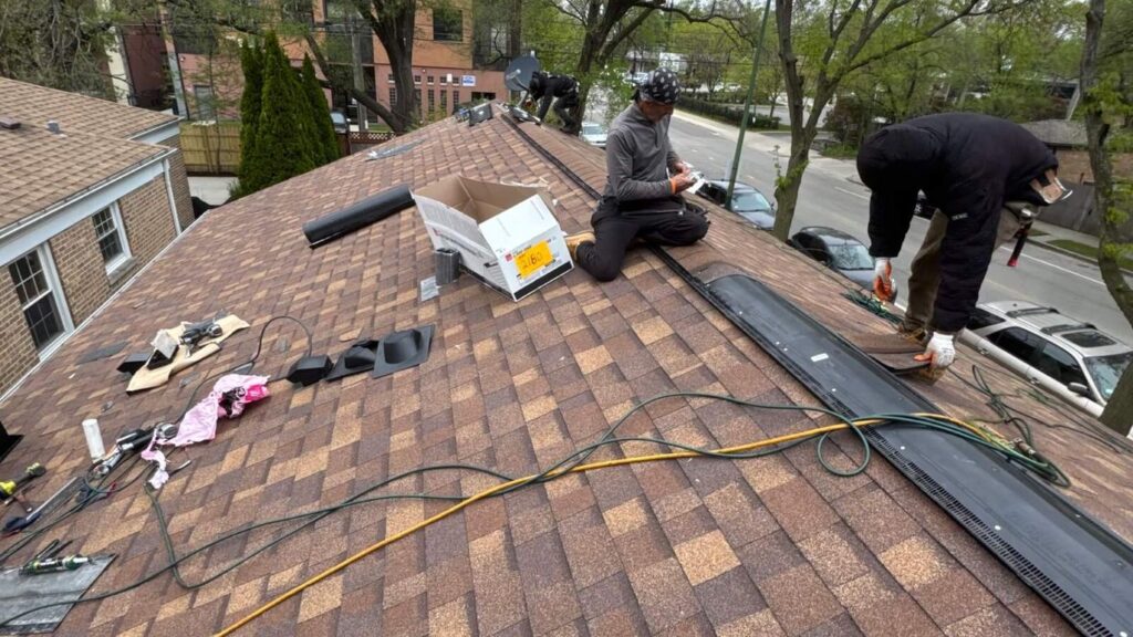 Two people working on a roof with shingles and tools.