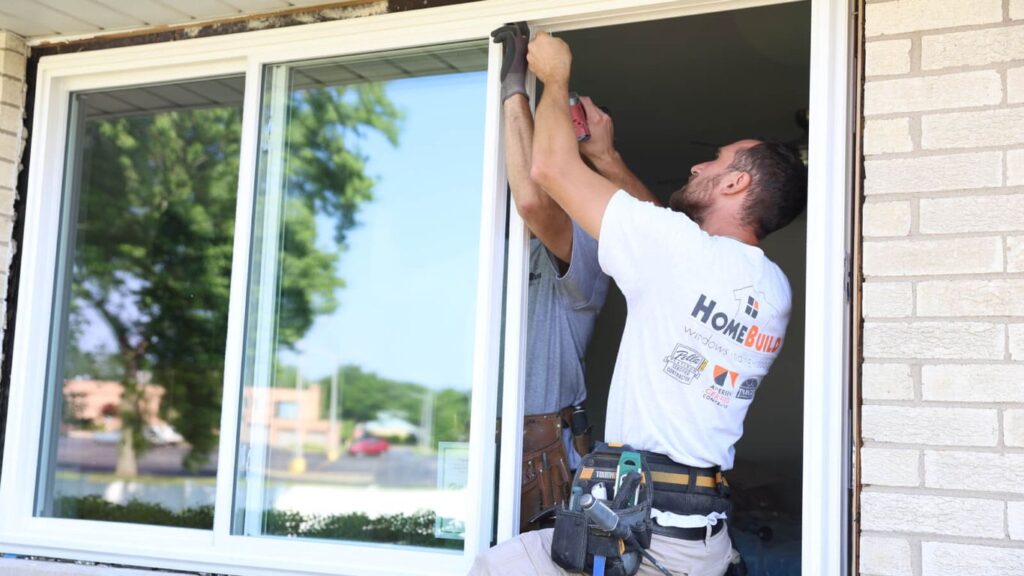 Workers installing a new sliding window on a brick house.